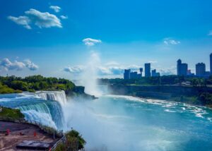 Breathtaking image of Niagara Falls with mist and cityscape under a clear blue sky.