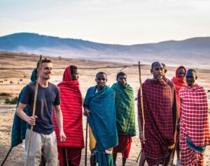 A traveler joins Masai tribe members on a sunny day in an open African landscape.